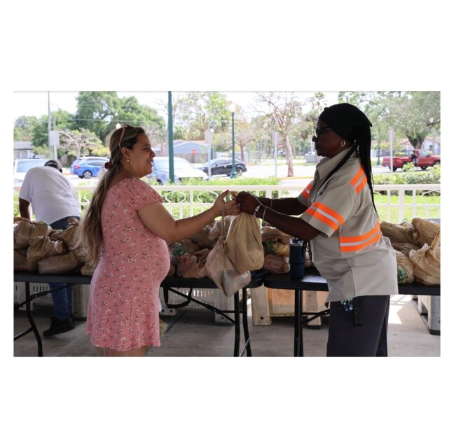 A Farm Share volunteer hands bags of groceries to a woman at a distribution
