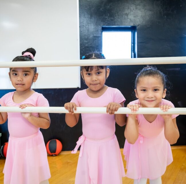 Three young dancers in ballet outfits at the barre during an RCMA dance class
