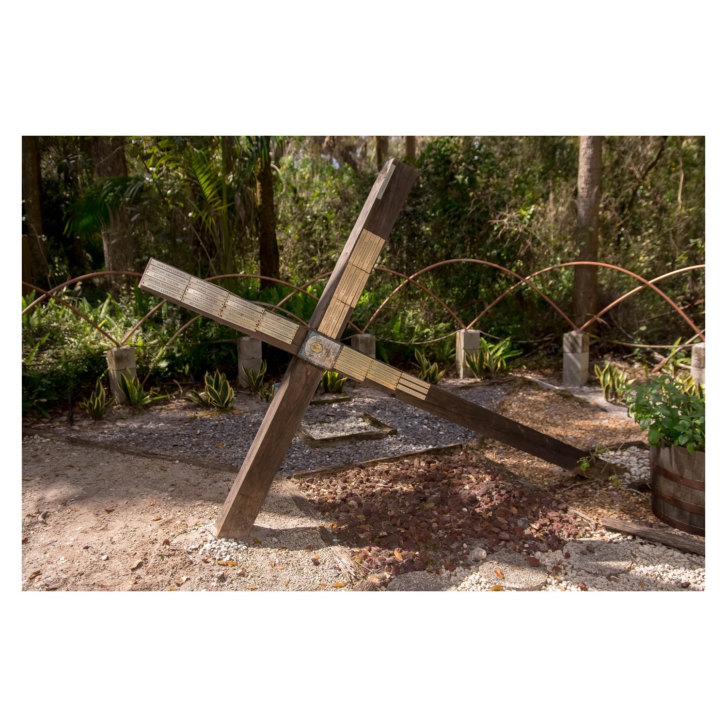 Wooden cross covered with engraved brass name plaques in a shaded garden