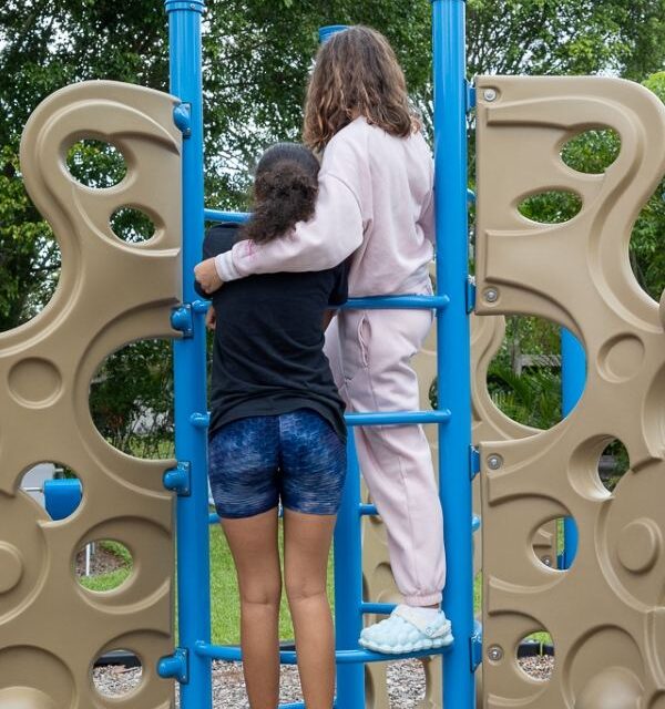 Two Youth Haven teens on a playground climbing structure, arms around each other