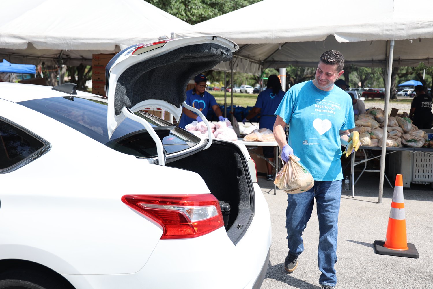 Volunteer carrying bags of produce to a waiting car at a food distribution