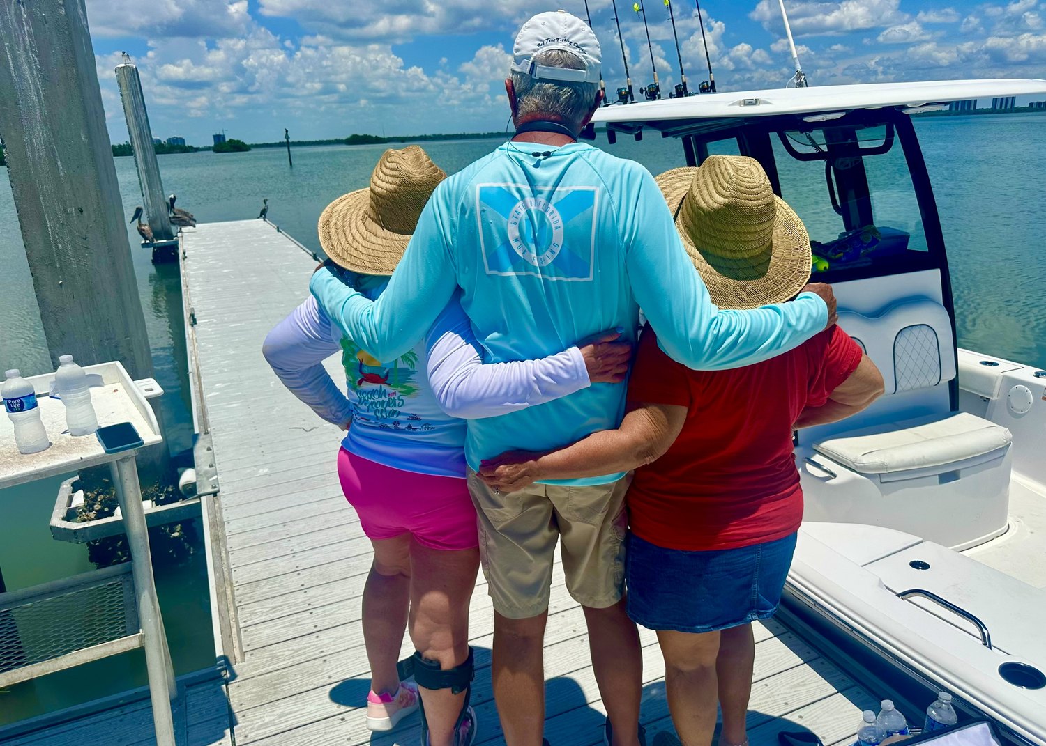 Captain and two guests in sun hats standing together on a boat at the dock