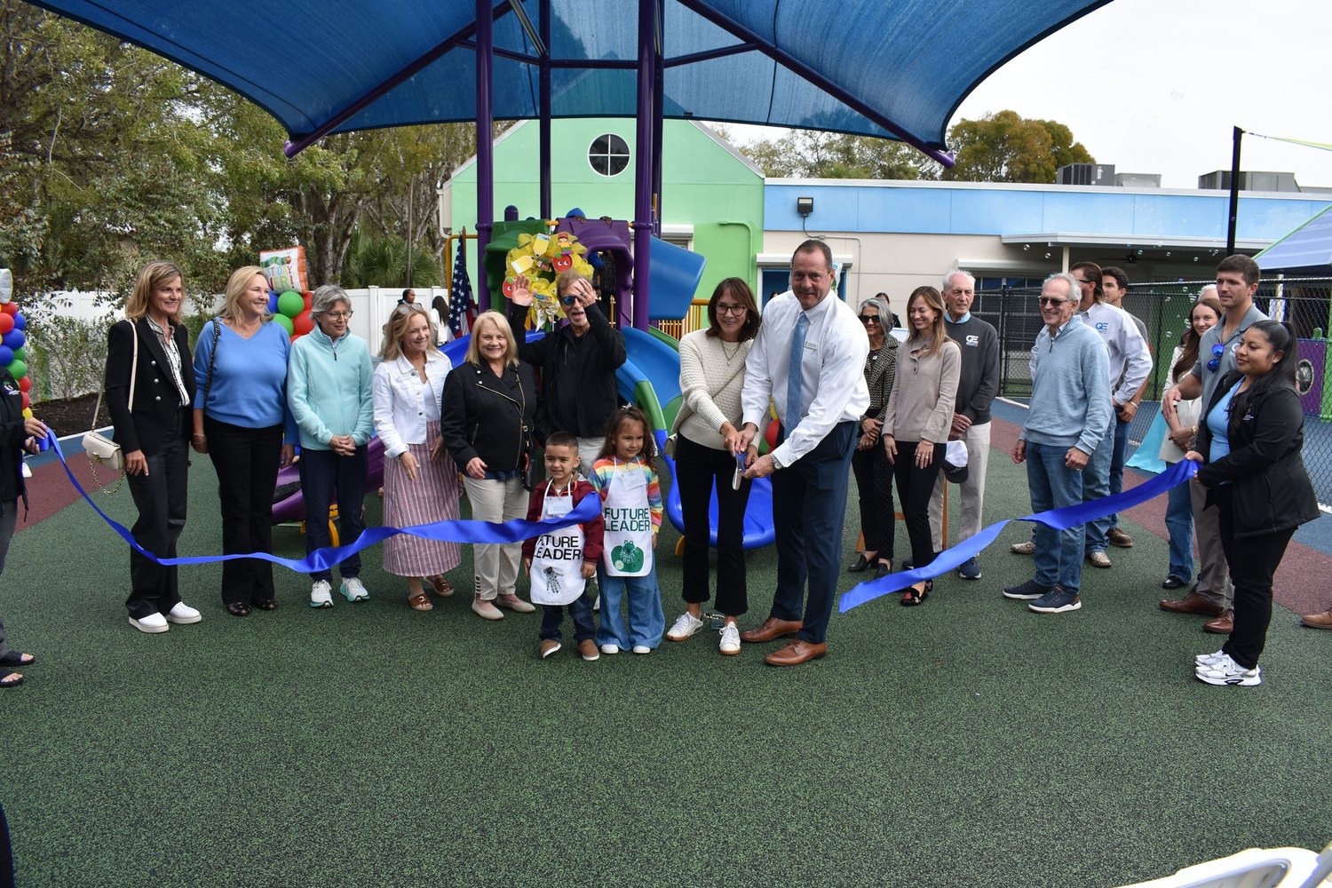 Group cutting a blue ribbon at the renovated Pathways playground with children