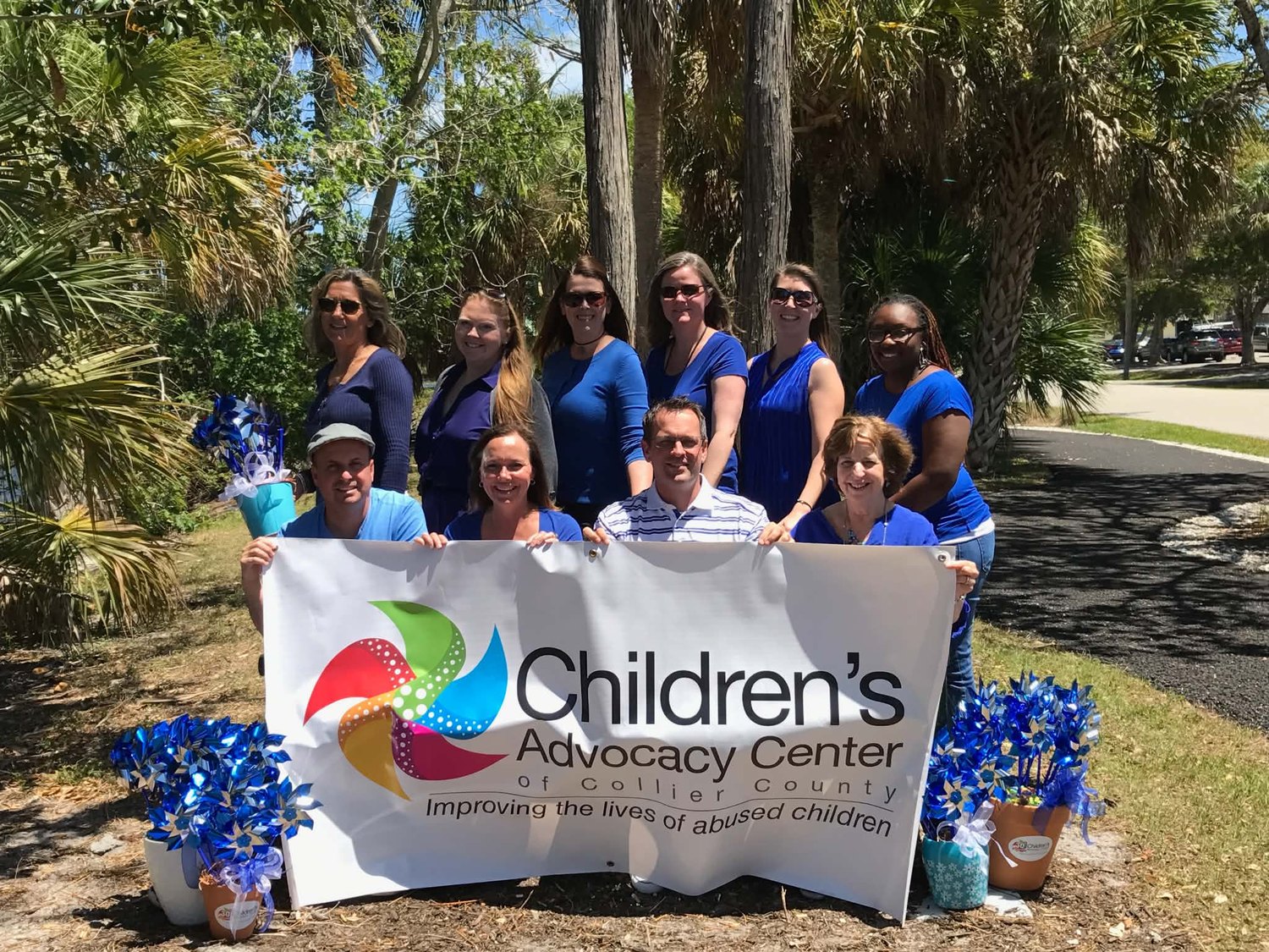 Collier CAC staff holding the Children’s Advocacy Center banner among blue pinwheels