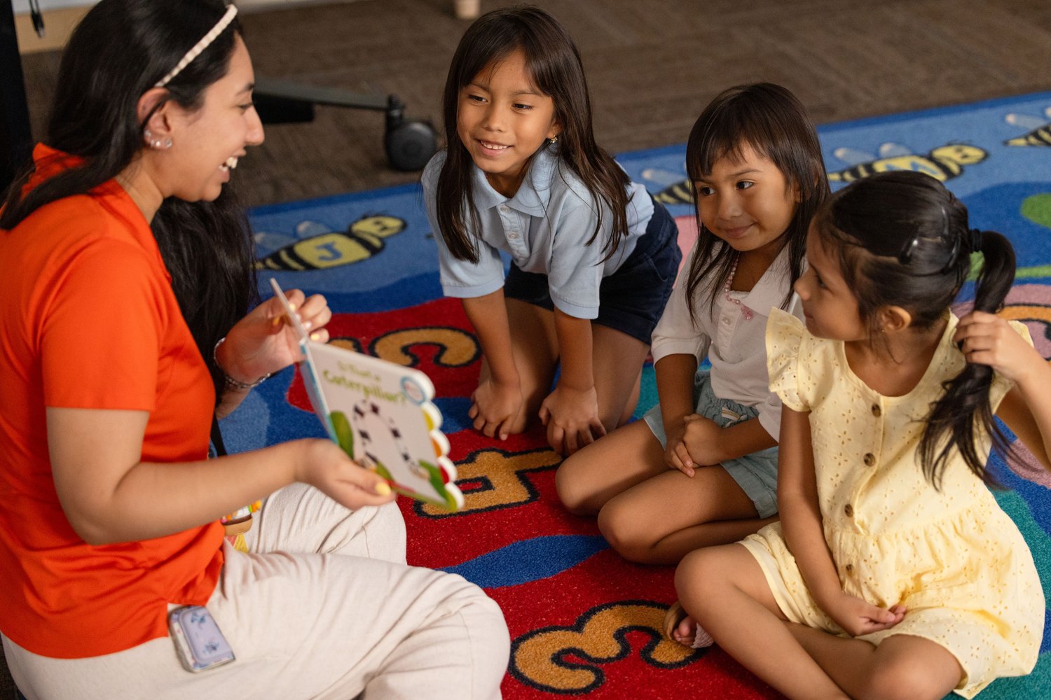 Teacher showing a lesson card to three young girls seated on a classroom rug