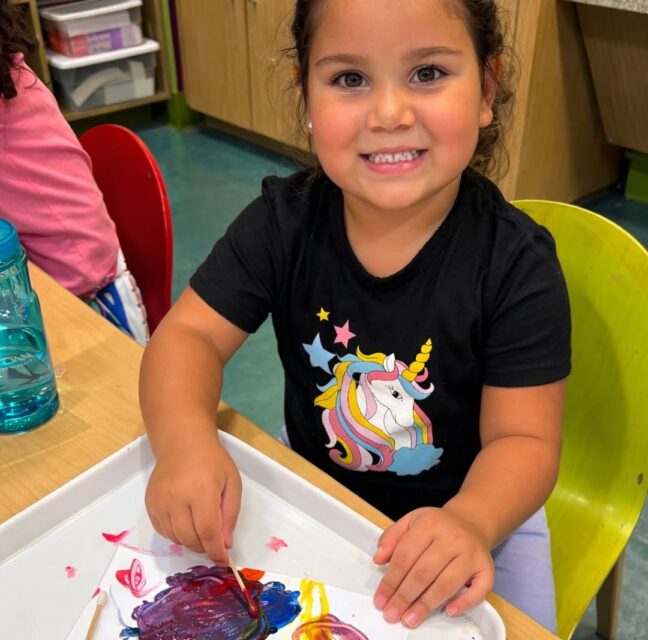 Young girl smiling while finger painting at a museum craft table
