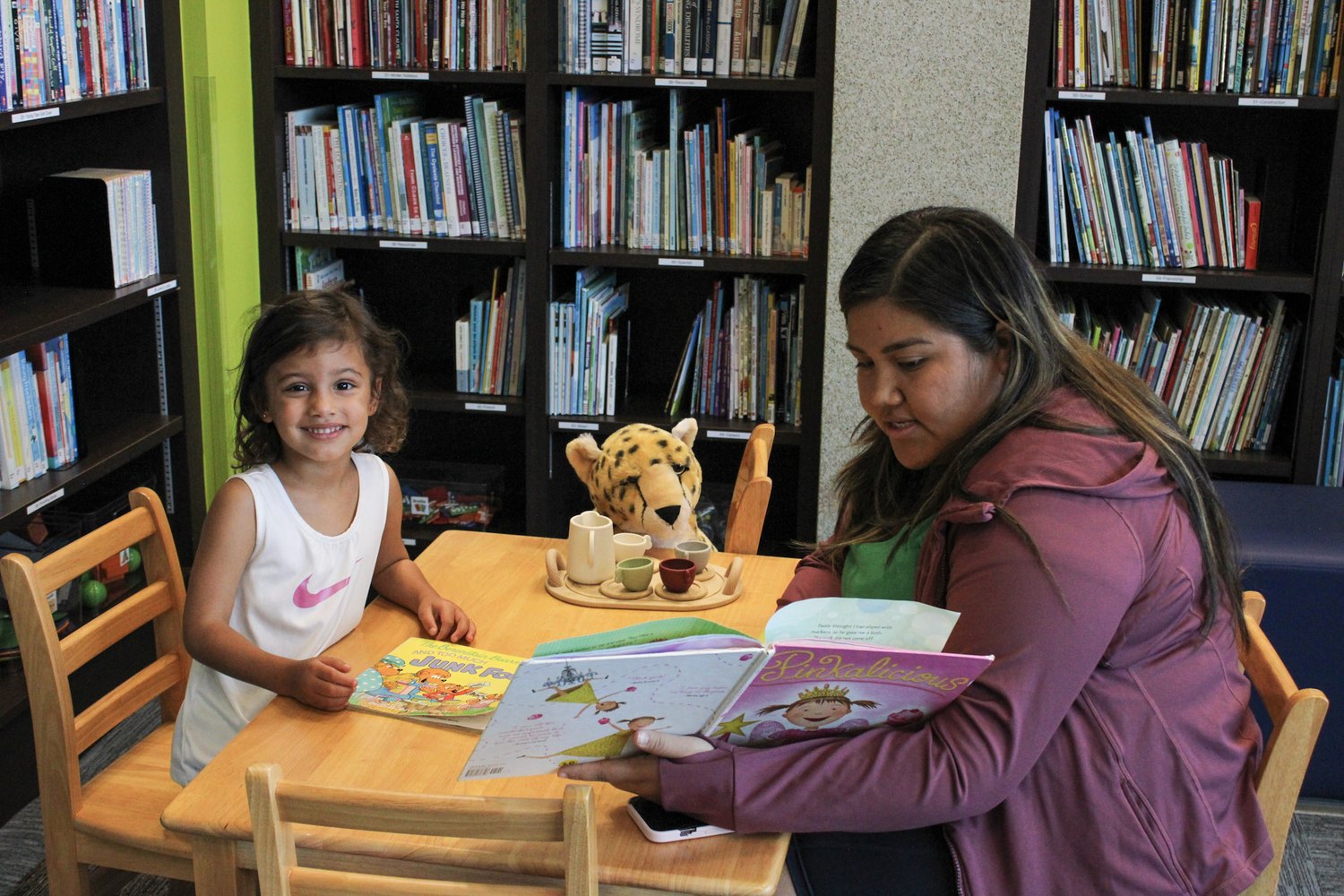 Girl and adult reading picture books together at a library table